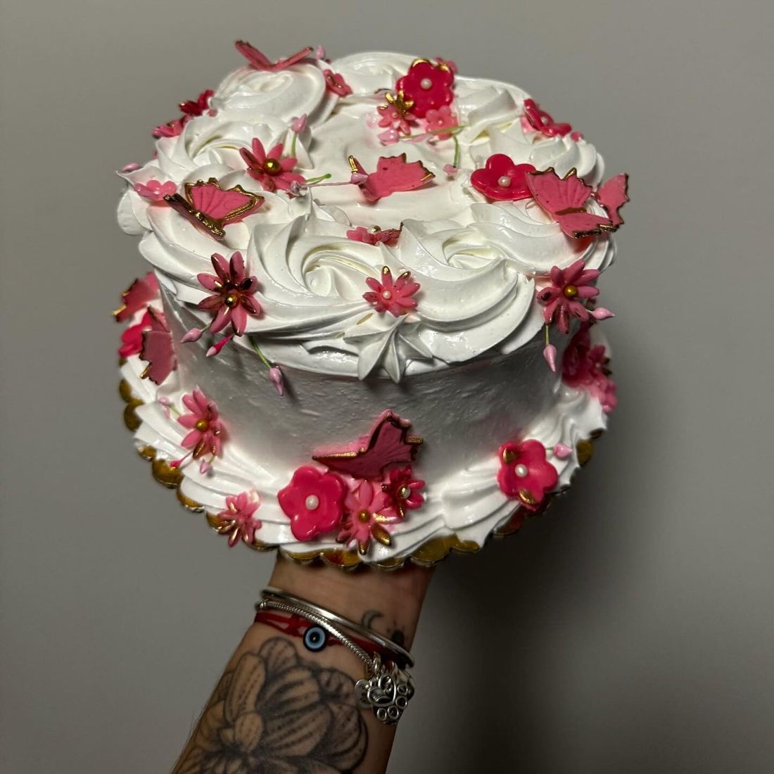 Mano tatuada de Alizon sosteniendo una torta con flores